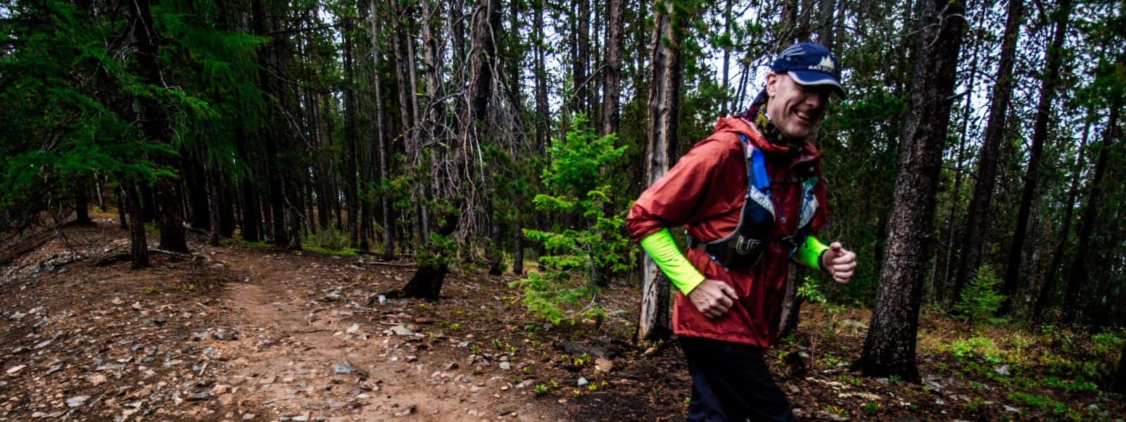 Coach JW smiling while running on a forest trail during an ultra trail race
